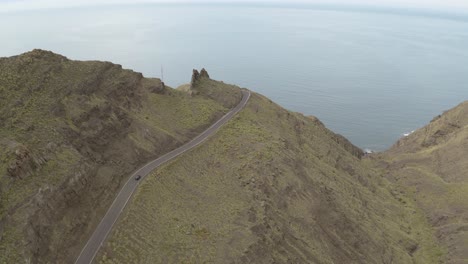 Panorama-Drohnenaufnahme-Eines-Autos,-Das-Durch-Eine-Straße-In-Den-Bergen-Und-Im-Meer-Im-Hintergrund-Fährt