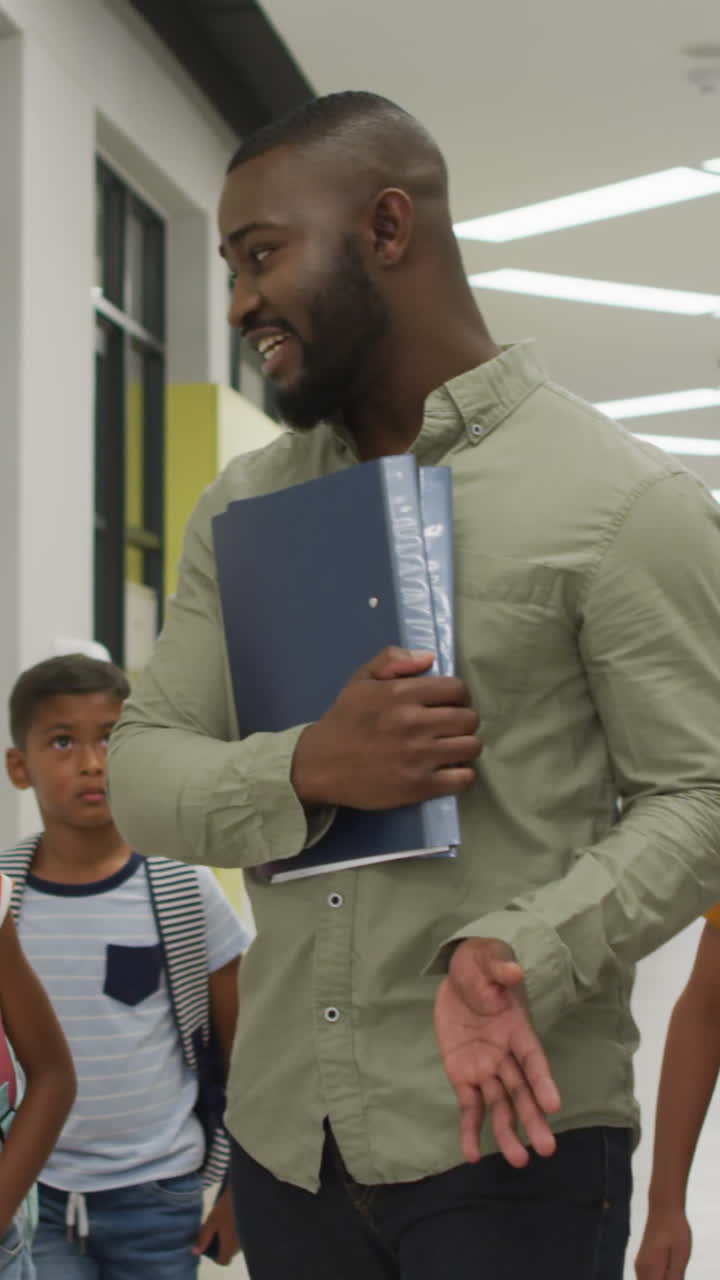 Video of happy african american male teacher and diverse pupils walking at school hall