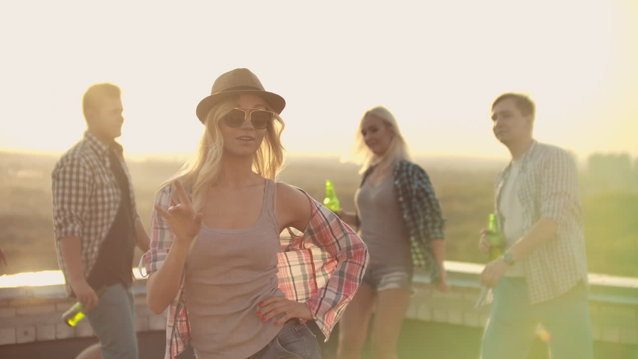 American girl moves beautifully in dance to music with her friends at a rooftop party. Her shirt and hair are scattered by body movements.