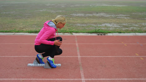 Vista-Lateral-De-Una-Atleta-Caucásica-Tomando-Posición-Inicial-En-La-Pista-De-Atletismo-En-El-Recinto-Deportivo-4k