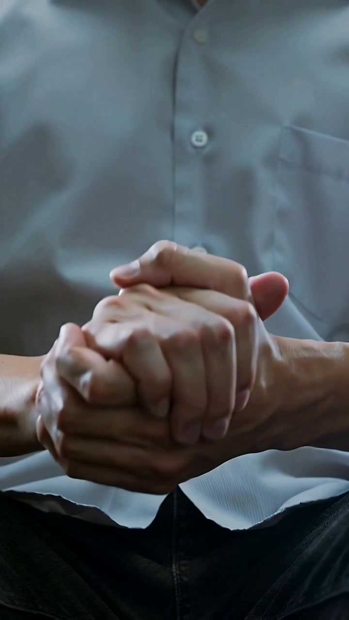 Video verticale: Uomo adulto seduto con camicia grigia che si massaggia i palmi delle mani in un angolo dell'ufficio.