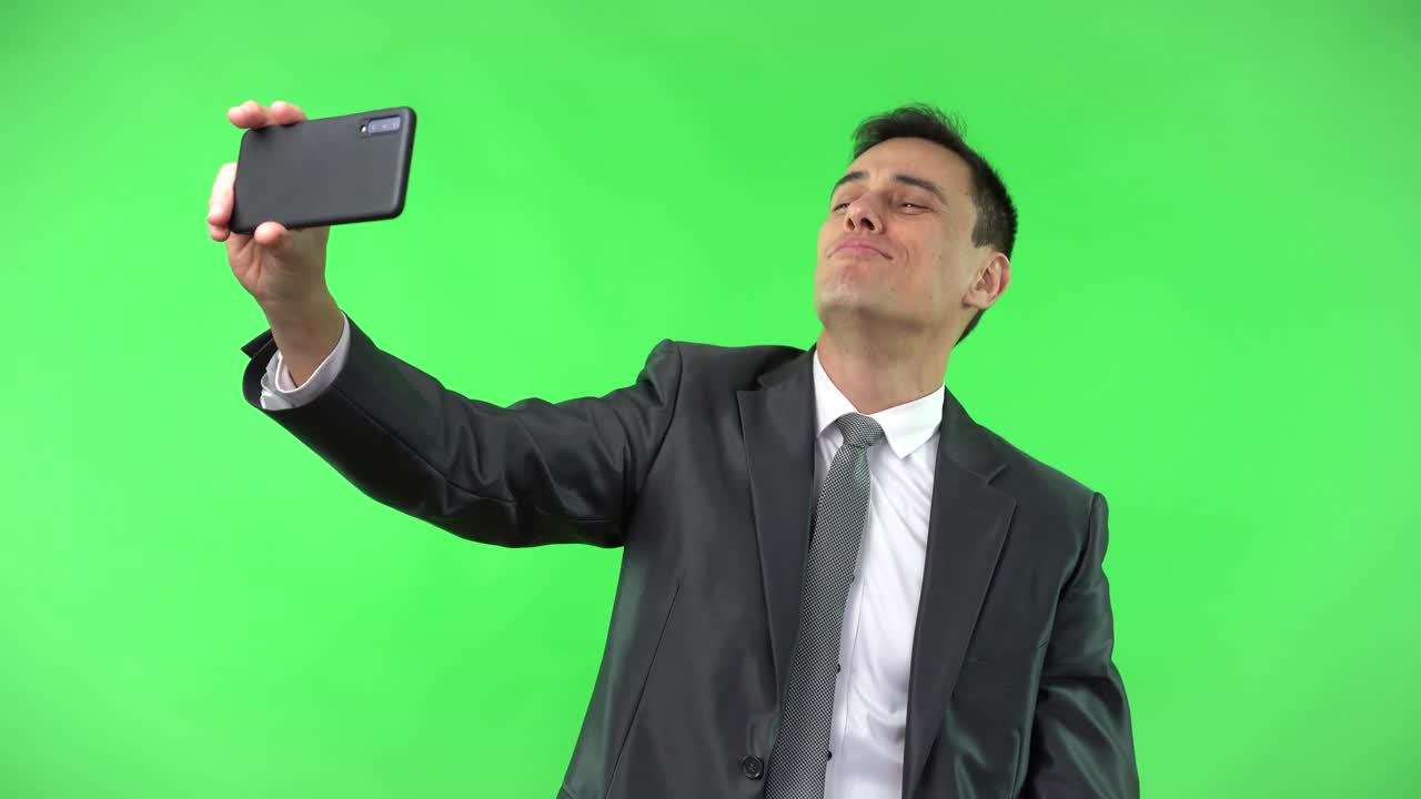 Man in Suit Takes Selfies with Smartphone on Green Screen