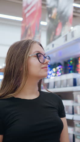 mujer navegando casualmente por el centro comercial, admirando las luces decorativas brillantes que parpadean en el fondo, las estanterías de las tiendas llenas de productos de iluminación festiva
