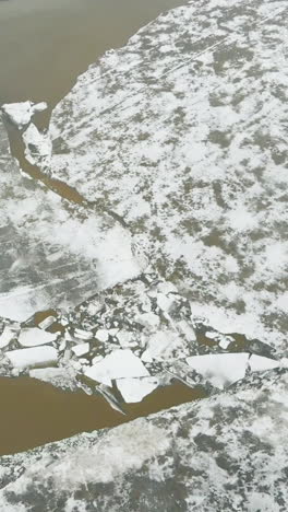 half frozen deep river at hilly bank with grey construction and modern bridge with driving cars aerial view
