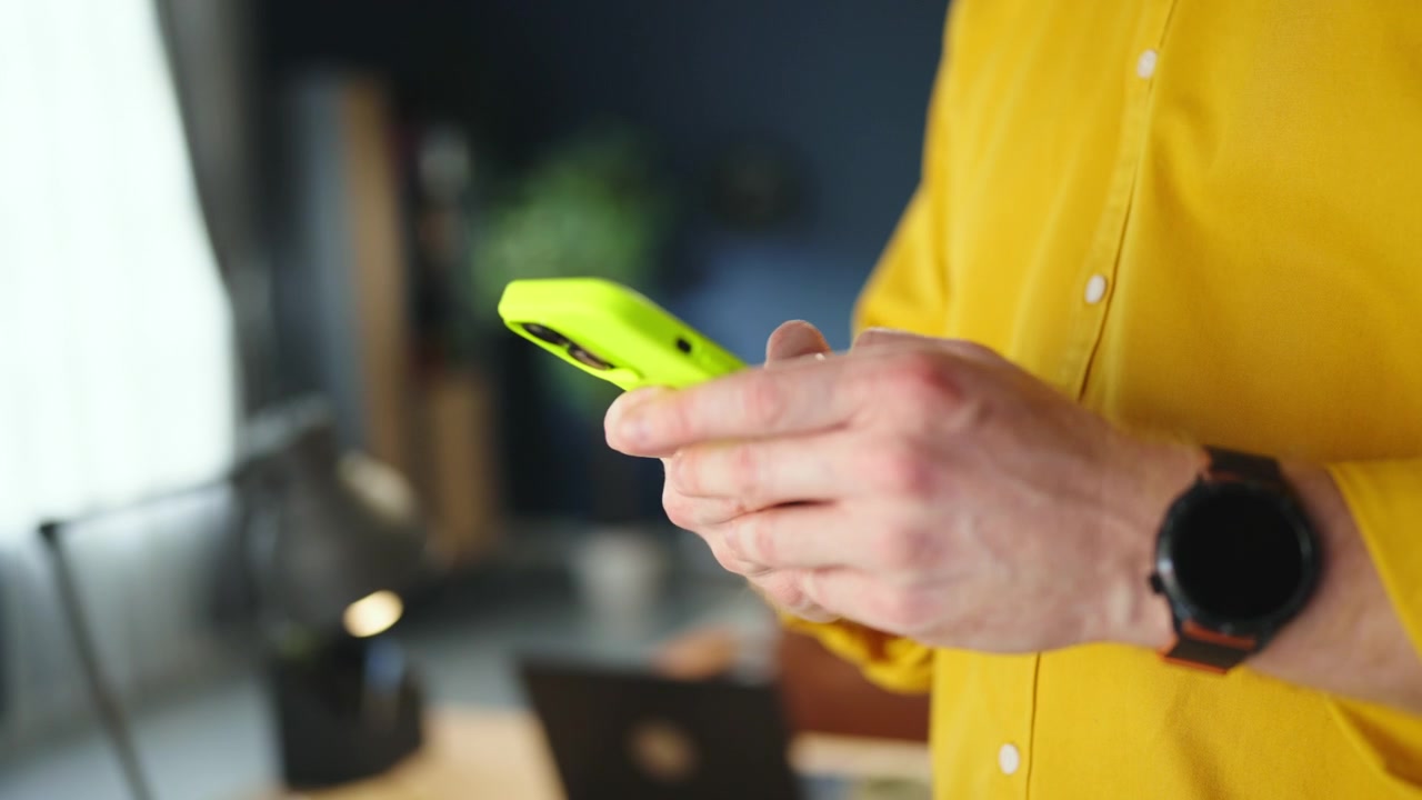 Uomo con camicia gialla che usa lo smartphone in ufficio