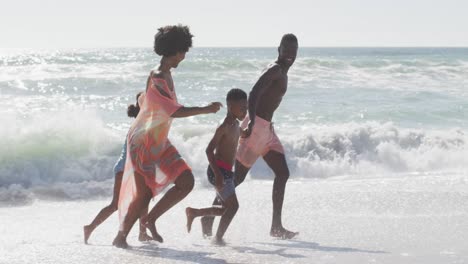 smiling african american family holding hands and running on sunny beach