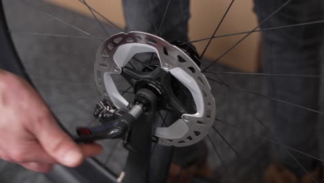 male hand of bicycle mechanic tightening wheel on bicycle fork with disc brakes using lever on thru-axle bolt