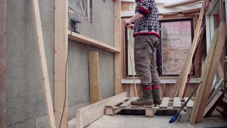 hombre midiendo la altura del soporte de madera para el estante dentro del invernadero