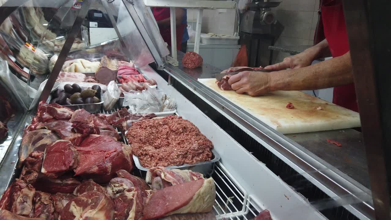tagliando la carne con un grosso coltello accanto al frigorifero pieno di carne bovina cruda mani tagliando da vicino tiro