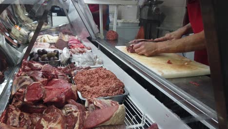 Cutting-Meat-with-big-knife-next-to-fridge-full-of-raw-beef-hands-cutting-close-up-shot