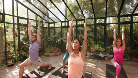 practicing yoga in glass house, group stretching on yoga mats in sunlight