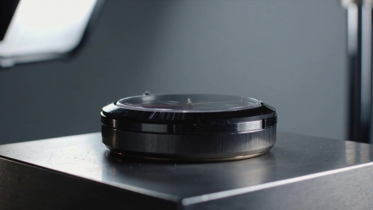La telecamera si avvicina, cassa di orologio nera che ruota su un piedistallo con softbox in studio, enfatizzando i dettagli.