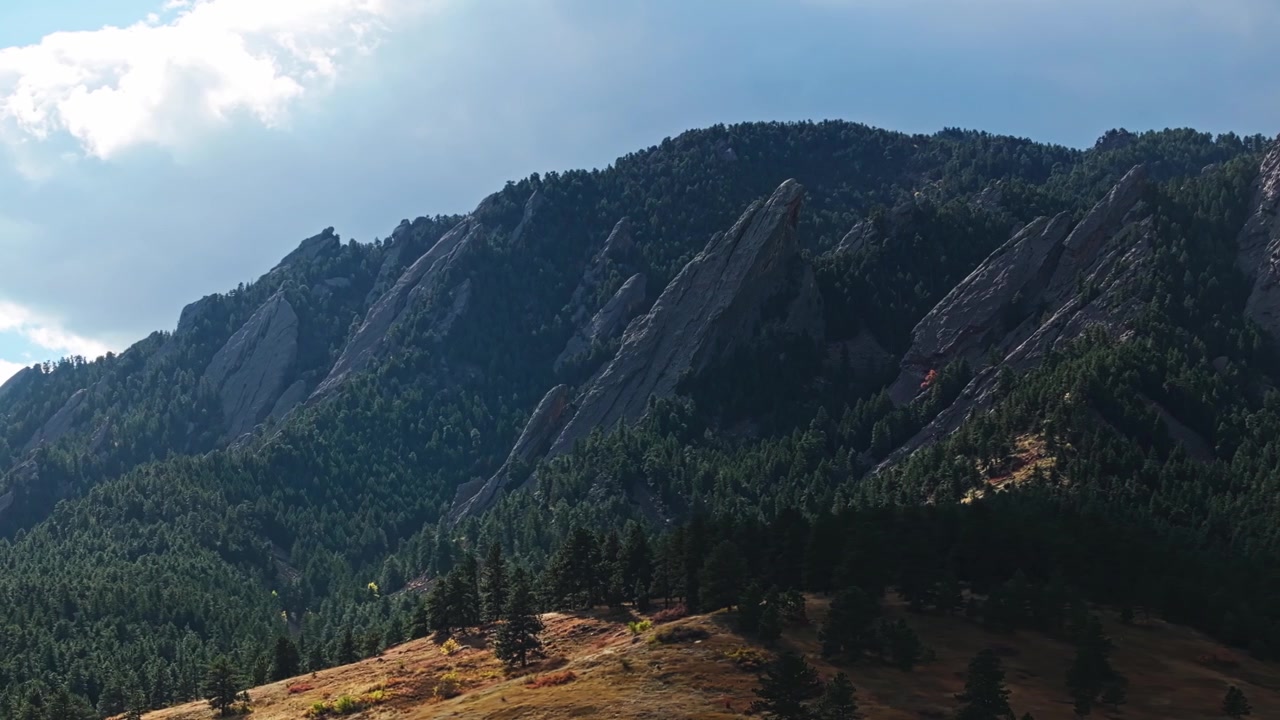 Telefoto udara Flatirons ikonik Boulder Colorado dengan pohon-pohon cemara yang menakjubkan, bergerak ke kiri.