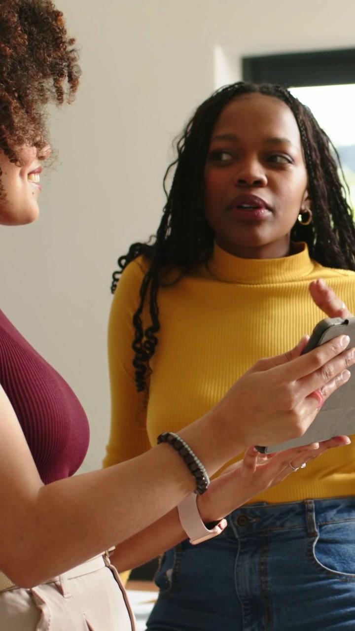Vertical video: Pointing maroon-top showing phone to yellow turtleneck at home, sharing notes