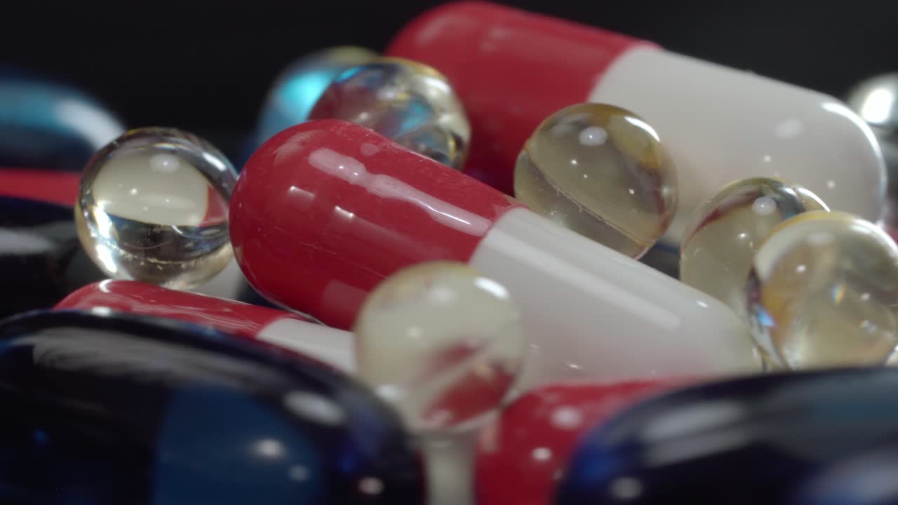 Close up of pharmaceutical capsules and transparent gel pills together on reflective surface