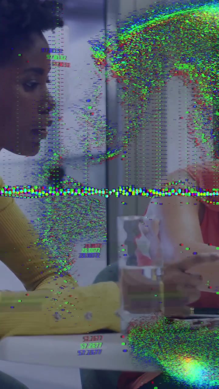 Vertical video: Left woman adjusting glass in meeting, causing digital glitch obscuring peer tablet