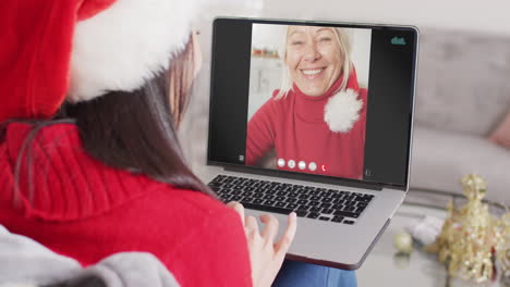 mujer caucásica con sombrero de santa teniendo llamada de video portátil con mujer caucácea