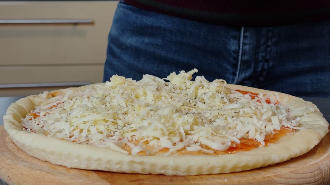 Sprinkling oregano on a freshly prepared pizza topped with grated cheese. A close-up of the pizza-making process, capturing the essence of homemade cooking and delicious Italian flavors.