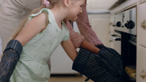 Kleines-Mädchen-Hilft-Mutter-Beim-Backen-In-Der-Küche,-Legt-Selbstgemachte-Kekse-In-Ofenhandschuhe-Und-Genießt-Frische,-Köstliche-Leckereien