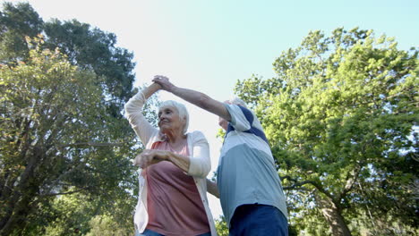 una pareja caucásica feliz bailando en un jardín soleado, en cámara lenta.