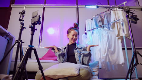 Waving in front of her online audience, a woman is promoting garments on a live online selling.