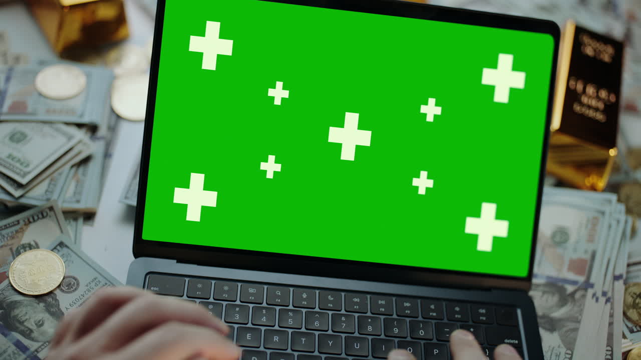 Laptop with green screen surrounded by money and gold