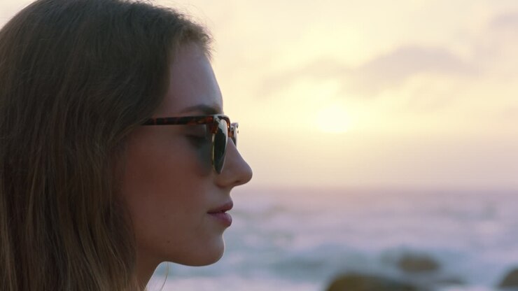 ritratto di una bella donna che si gode la tranquillità del mare al tramonto esplorando la spiritualità guardando in alto pregando contemplando il viaggio rilassandosi sulla spiaggia indossando occhiali da sole