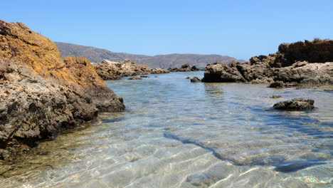 shallow clear sea waters on rocky coast, sunny day, low angle static