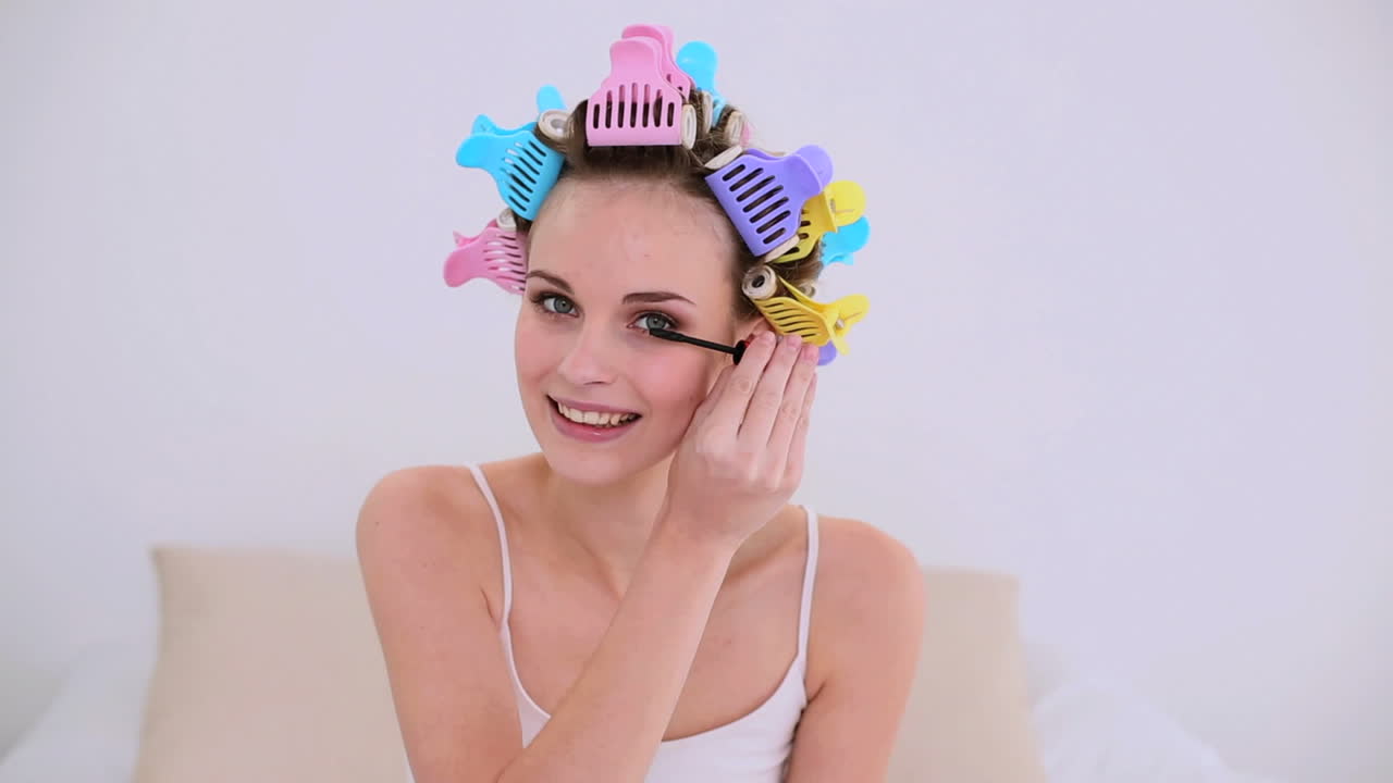 머리 롤러 를 입은 젊은 모델 이 마스카라 를 쓰고 있다