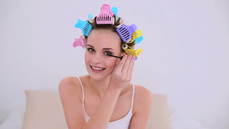 joven modelo en rodillos de cabello poniéndose máscara