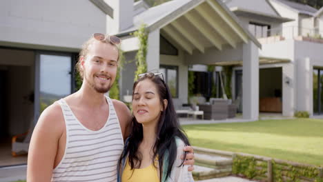 A-young-biracial-couple-smiles-by-their-poolside-home,-copy-space