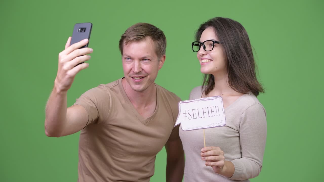 Young happy couple taking selfie together against green background