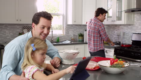 Girl-uses-tablet-in-kitchen-with-parents,-dad-holding-baby