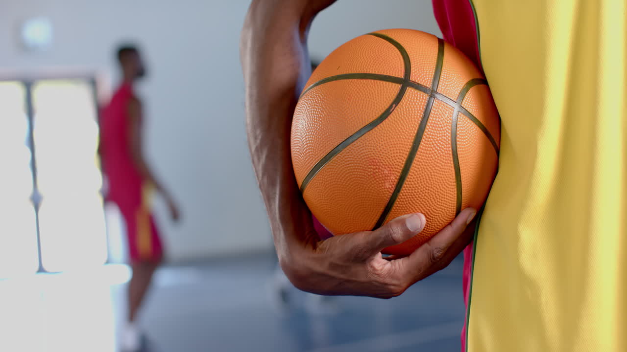 primer plano de una pelota de baloncesto sostenida por un hombre afroamericano