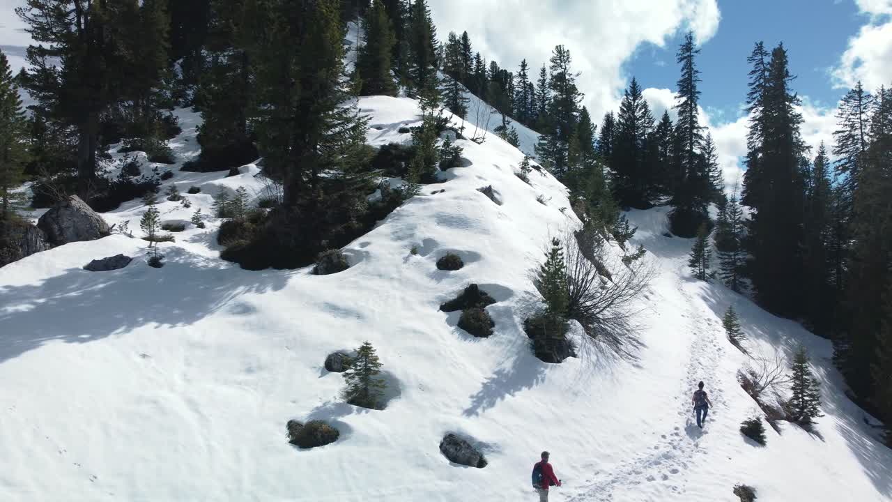 Two persons man and woman hike trek on an epic snow mountain panorama path high above scenic Bavaria Elmau castle and glacier peaks in the Bavarian Austrian alps on a cloudy and sunny day in nature