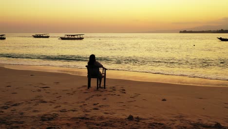 chica solitaria viendo hermosos colores crepusculares con cielo amarillo reflejando sobre la tranquila laguna lavando arena de playa exótica en bali