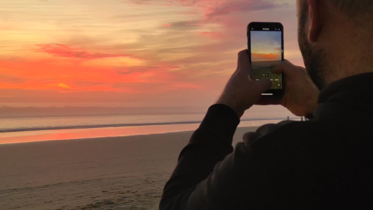 joven turista toma fotos, graba video de la puesta de sol en la playa con un teléfono inteligente moderno