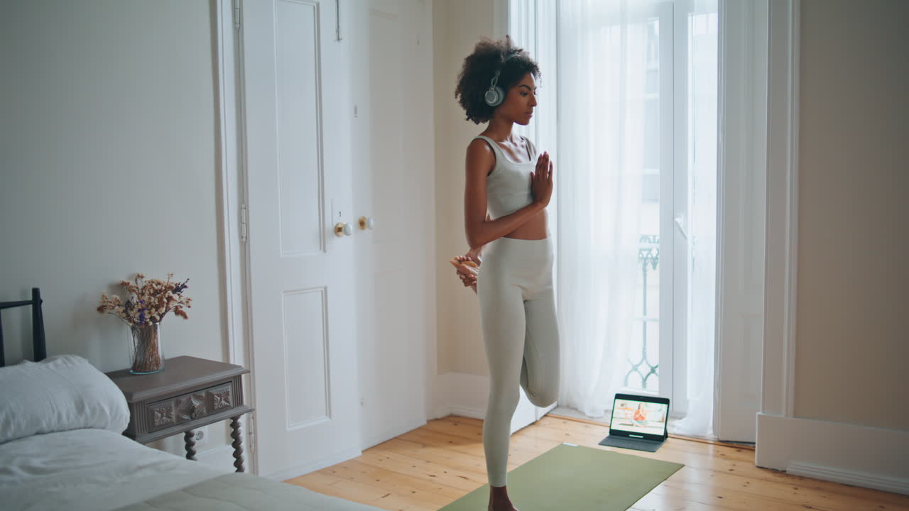 Modella in forma che esegue asana yoga in camera da letto. Ragazza dalla pelle scura che allena la flessibilità.