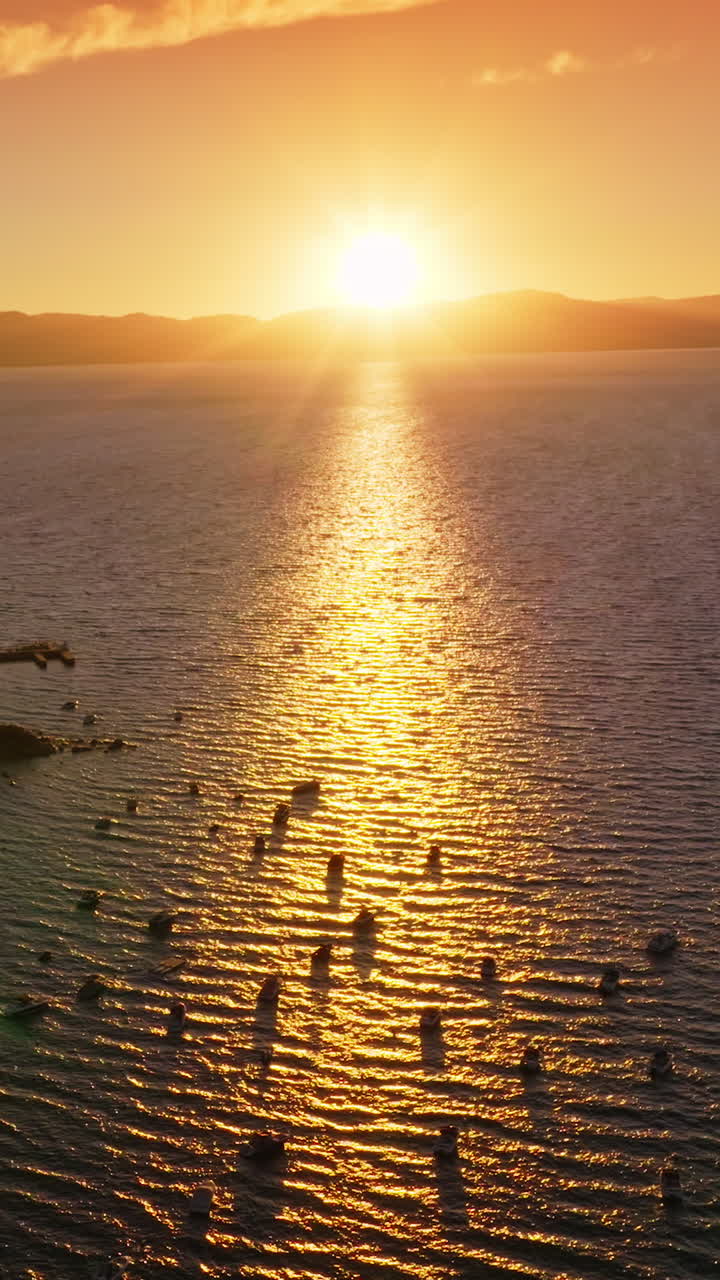 Sailing boats on the water of Lake Tahoe enjoying the stunning sunset. Beautiful scenery of the lake in the rays if setting sun. Mountains at backdrop. Vertical video
