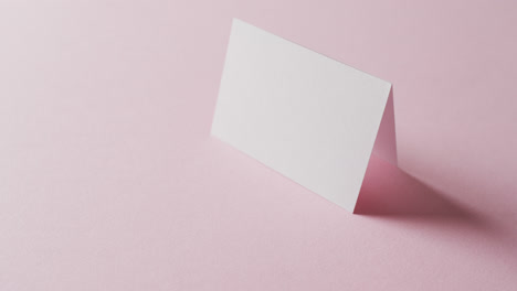 close up of two blank white business cards on pink background, copy space, slow motion