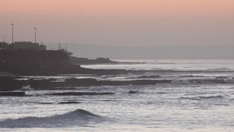 Sunrise-rising-over-the-cliffs-with-waves-crashing-in-the-dusk-of-early-morning