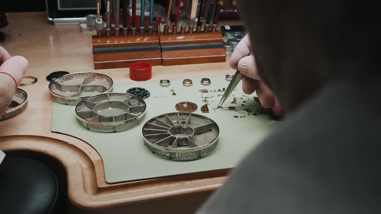 A watchmaker carefully putting tiny parts of a wristwatch into a metal screen container for cleaning - close up
