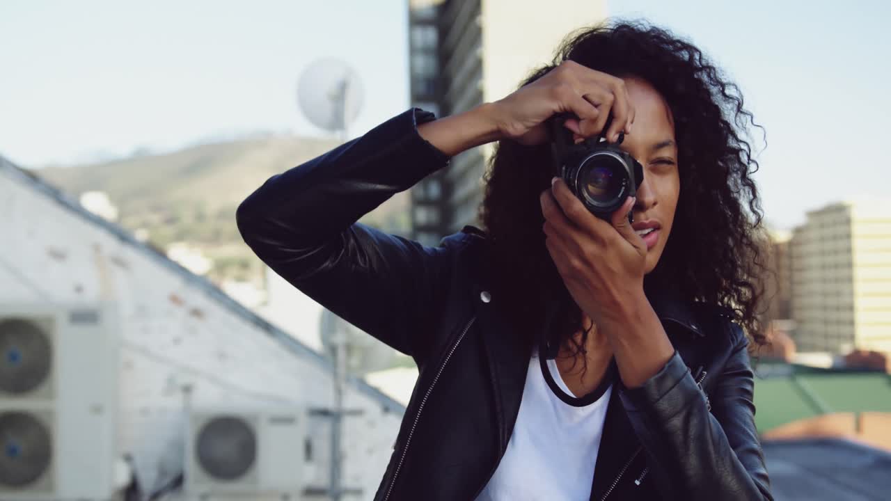 Fashionable young woman on urban rooftop taking photos
