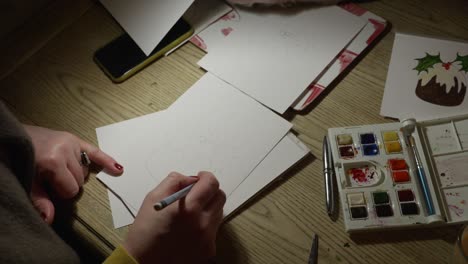 A-medium-shot-of-female-hands-sketching-a-Christmas-card,-preparing-to-paint