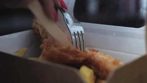 Close-up-of-woman-cutting-into-fish-and-chips-with-wooden-knife