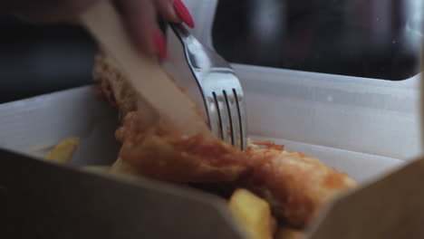 cerca de una mujer cortando pescado y patatas fritas con un cuchillo de madera