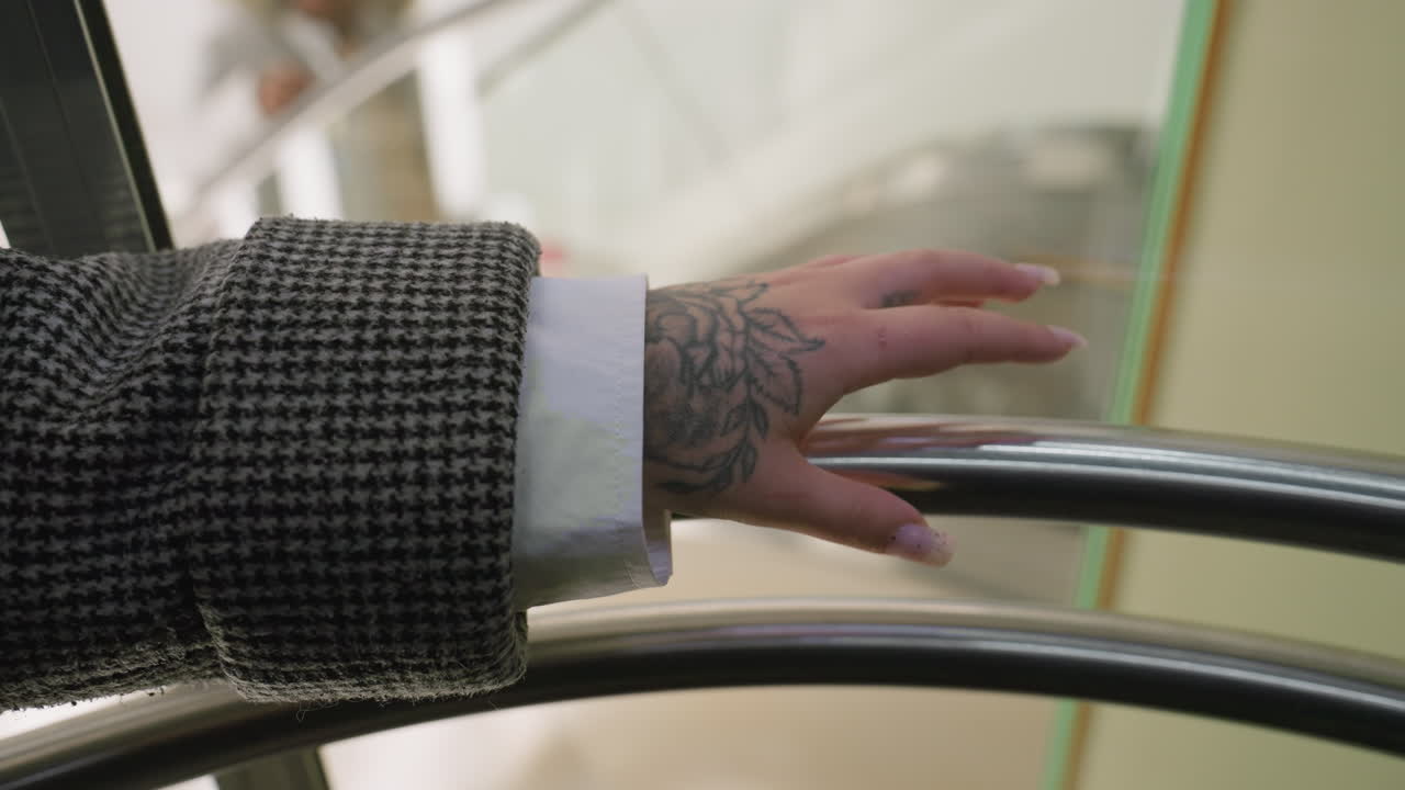 close up of tattooed hand gently tapping shiny iron rail with soft focus on background seen through transparent panel inside modern indoor setting creating mood of stillness