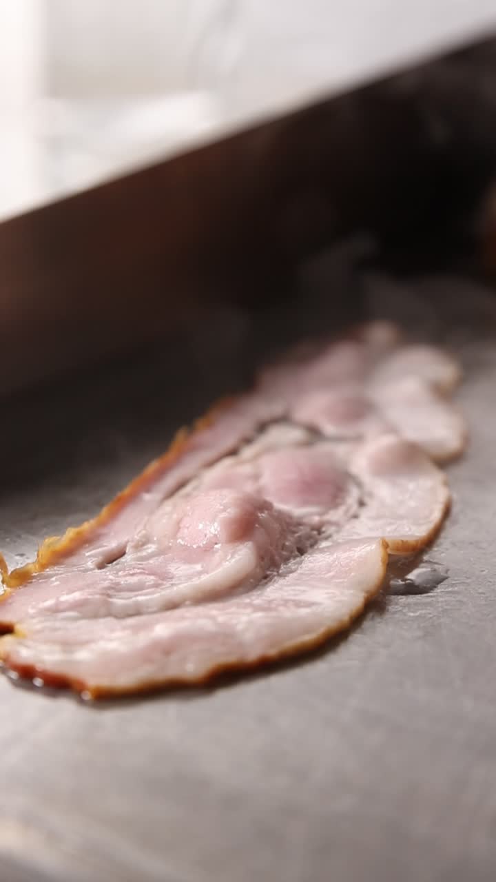 Primo piano di bacon che sfrigola su una piastra calda