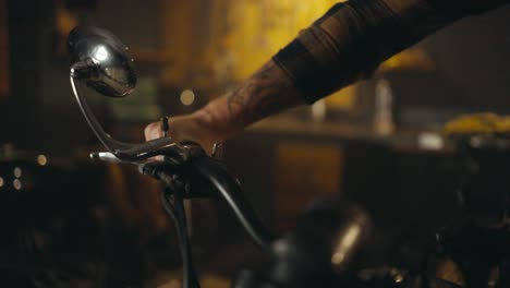 close up, a bike guy in a checkered shirt holds on to the handlebars of a motorcycle and takes it out of his garage workshop with many tools
