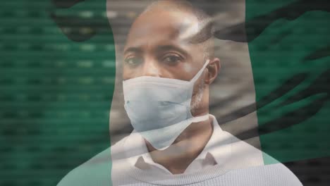 Animation-of-flag-of-nigeria-waving-over-african-american-man-wearing-face-mask-in-city-street